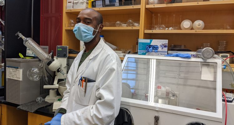 Dr. Delwin Elder in the NLM Photonics wet chemistry lab. He wears a white lab coat and blue gloves.