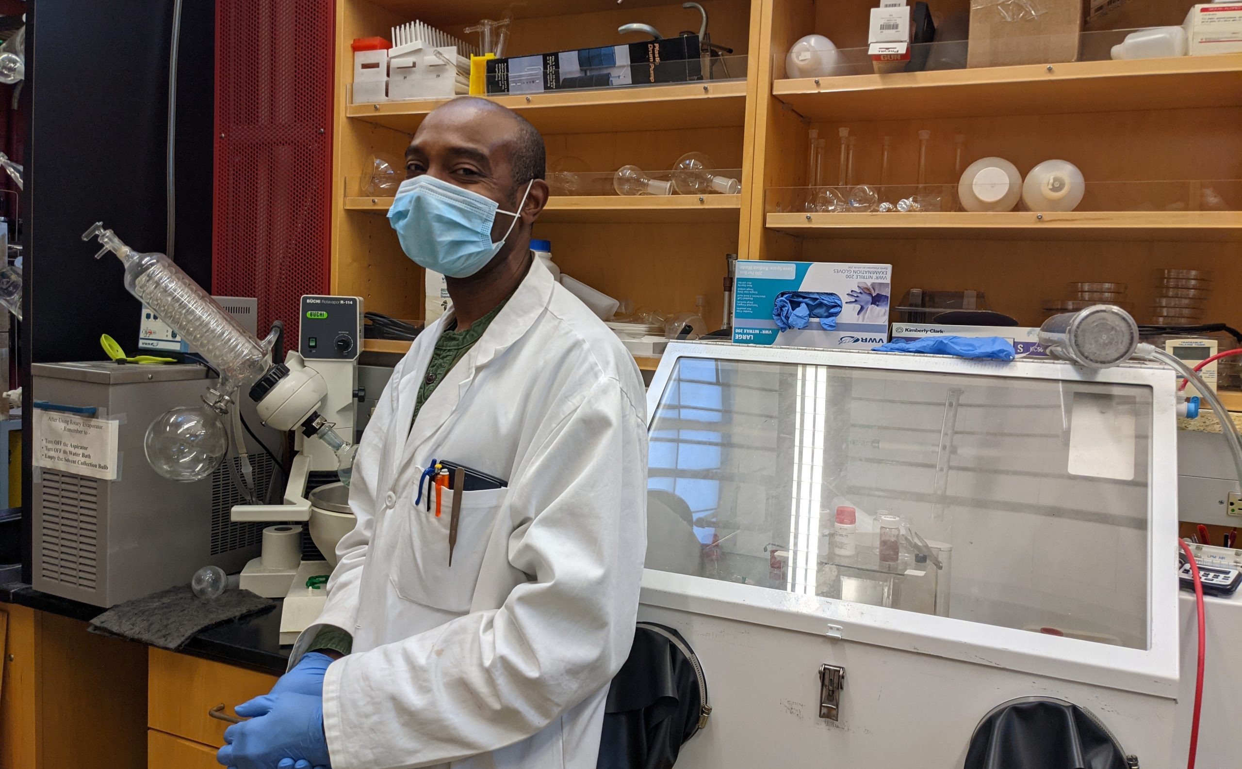 Dr. Delwin Elder in the NLM Photonics wet chemistry lab. He wears a white lab coat and blue gloves.