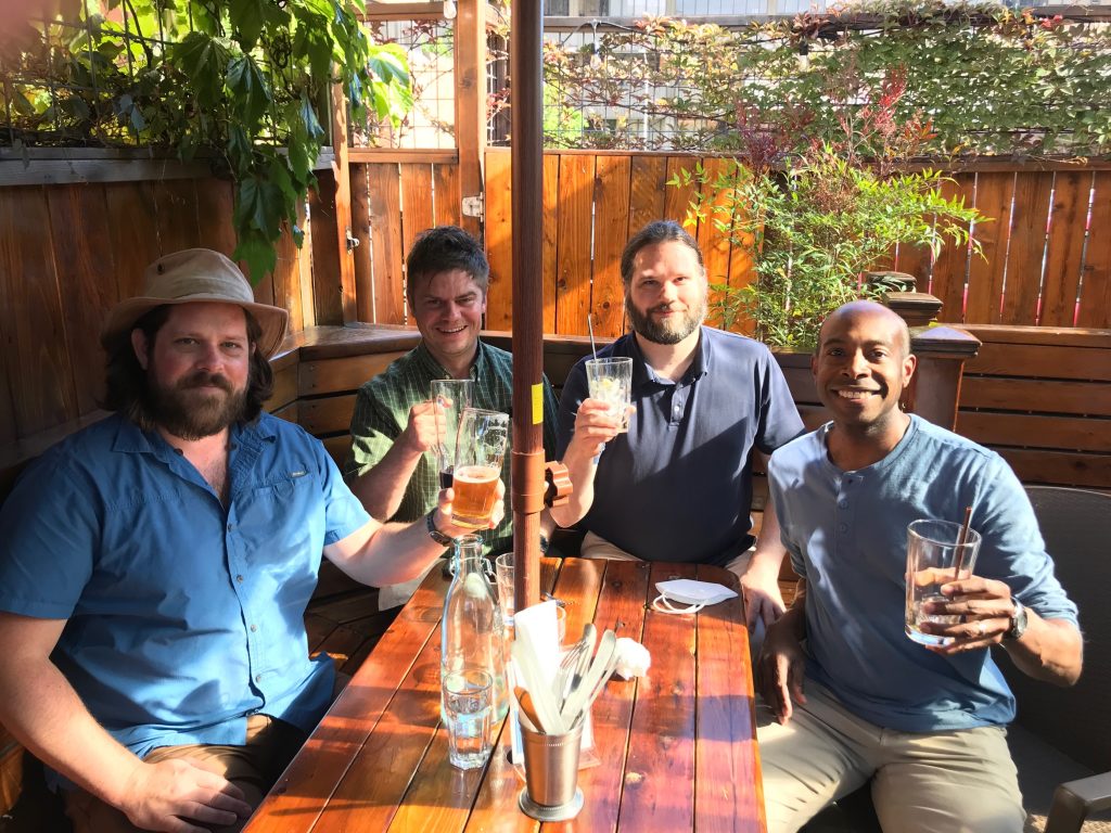 Drs. Kevin O'Malley, Lewis Johnson, Scott Hammond, and Delwin Elder around a wooden table outside and having a toast about the wafer