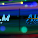 On left is NLM's blue logo, there's a divider in the middle, and on the right is AIM Photonics' blue logo with yellow starburst. The background is multi-colored lights from cables in a data center