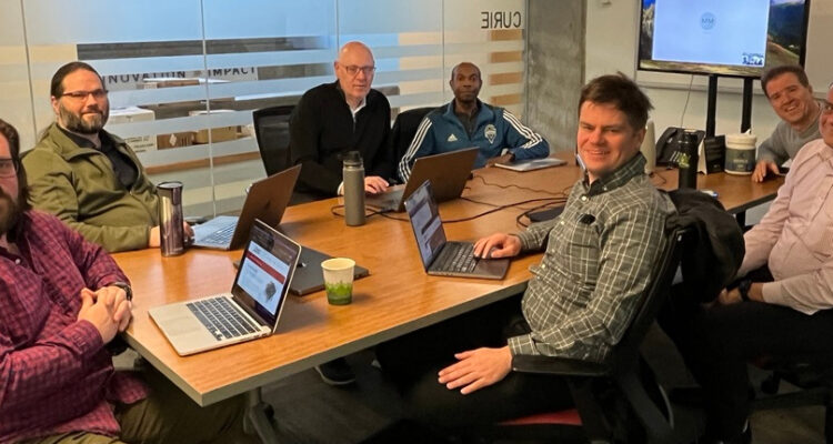 The team gathered around a table with Marion the video call. L-R Kevin, Scott, Gerard, Delwin, Lewis, David, and Vijay